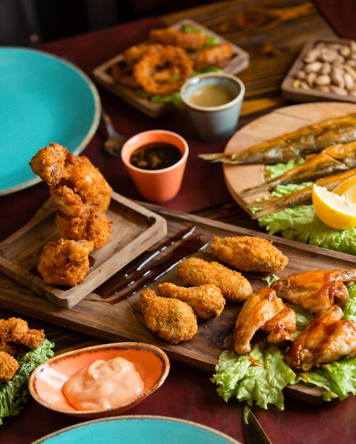 Crujientes nuggets de pollo y barbacoa con salsas y hierbas en una bandeja de madera con platos azules alrededor.