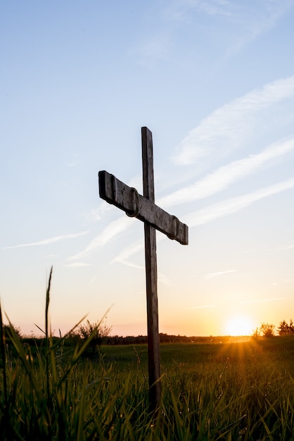 Cruz de madera en un campo de hierba con el sol brillando en un cielo azul