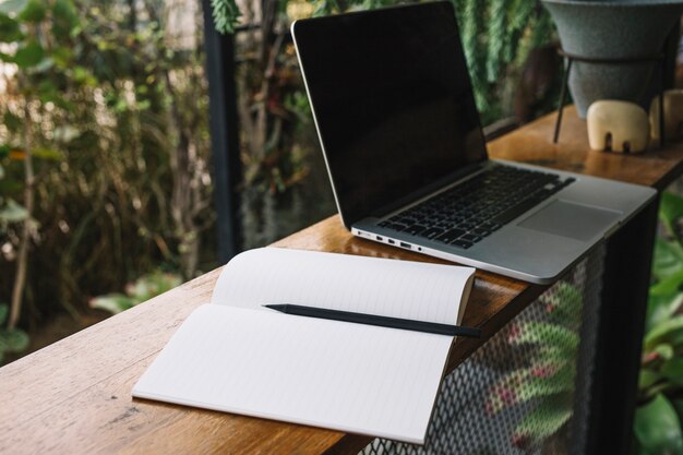 Cuaderno abierto cerca de la computadora portátil en el jardín