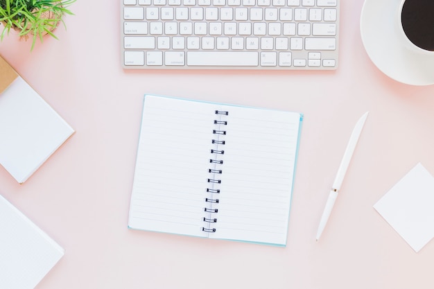 Foto gratuita cuaderno abierto cerca del teclado y la taza de café en el escritorio rosa