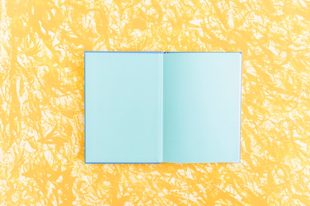 Un cuaderno abierto de páginas azules sobre fondo amarillo con textura