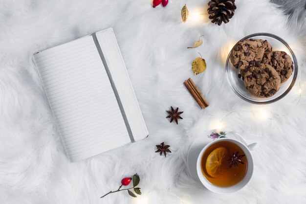 Cuaderno abierto en plaid cerca de té con galletas