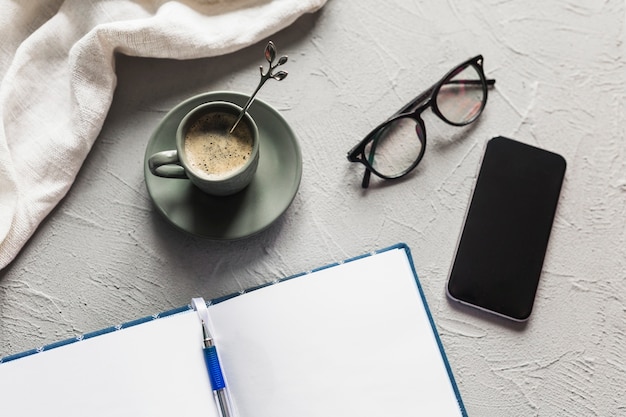 Cuaderno abierto con taza de café y teléfono inteligente