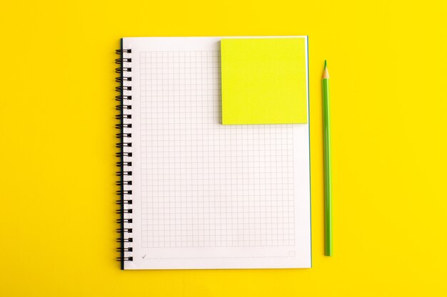 Cuaderno abierto de vista frontal con adhesivo amarillo sobre escritorio amarillo
