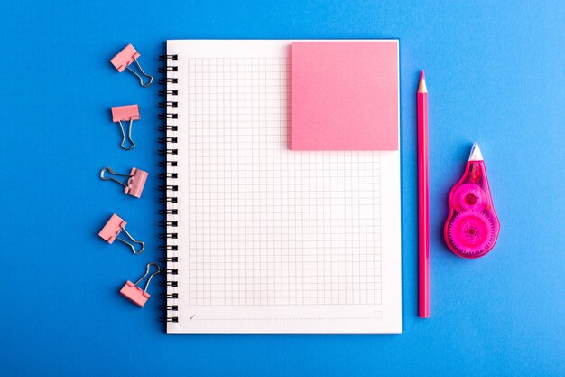 Cuaderno abierto de vista frontal con pegatina rosa en el escritorio azul