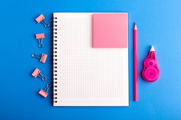 Cuaderno abierto de vista frontal con pegatina rosa en el escritorio azul