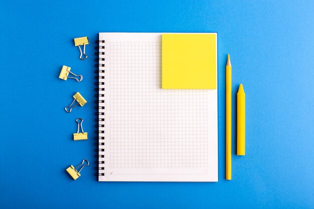 Cuaderno abierto de vista frontal con pegatinas y lápiz sobre la superficie azul