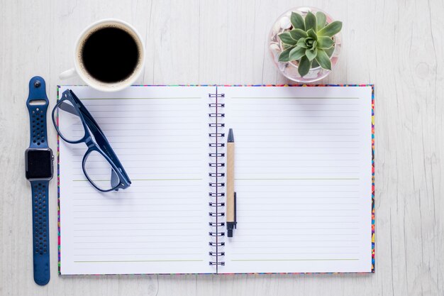 Cuaderno y accesorios cerca del café y la planta