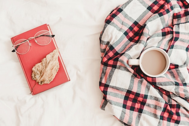 Cuaderno con anteojos y hojas en él cerca de bebida caliente en cuadros