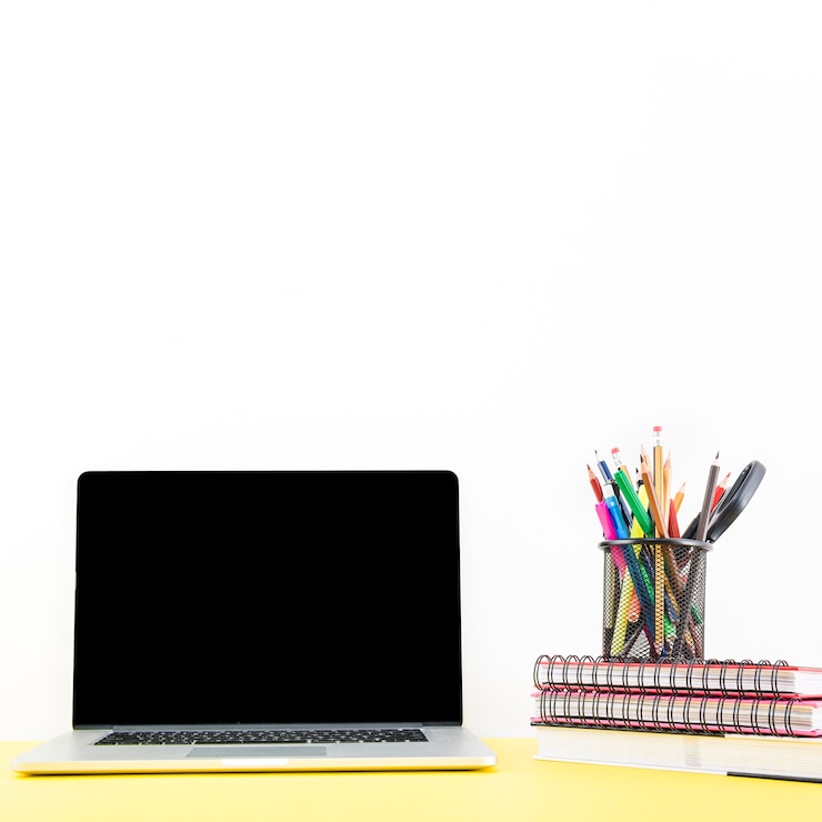 Foto gratuito cuaderno apilado con varias plumas y lápices en el titular cerca de la computadora portátil en el escritorio
