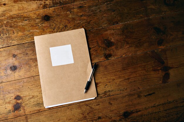 Cuaderno artesanal sin etiqueta y un bolígrafo de plástico negro sobre una vieja mesa de madera con textura
