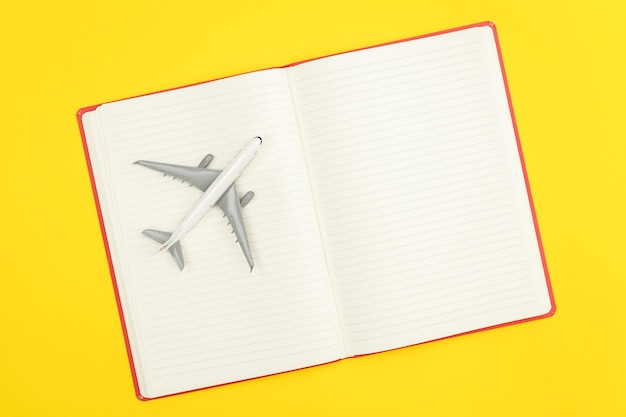 Foto gratuita cuaderno en blanco y modelo de avión sobre fondo amarillo plano