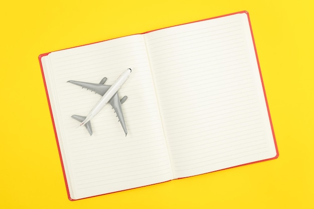 Cuaderno en blanco y modelo de avión sobre fondo amarillo plano