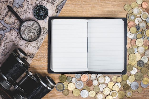 Cuaderno en blanco con monedas y objetos de viaje