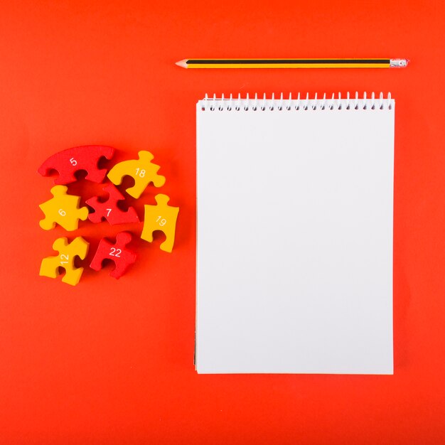 Cuaderno en blanco con rompecabezas en la mesa roja