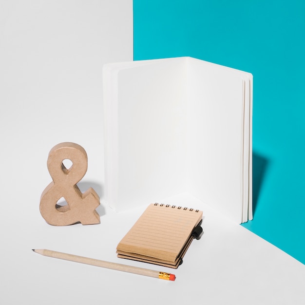 Foto gratuita cuaderno en blanco símbolo ampersand; lápiz; y bloc de notas de espiral en el fondo