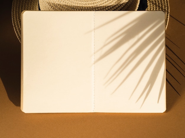 Cuaderno blanco sobre una sombra de sombrero y hoja de palma