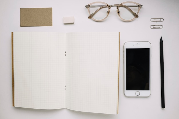 Cuaderno de bocetos abierto cerca de teléfonos inteligentes y gafas