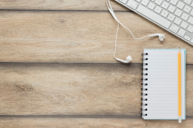 Cuaderno con bolígrafo cerca de teclado y auriculares en mesa de madera