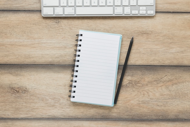 Cuaderno con bolígrafo cerca del teclado en la mesa de madera