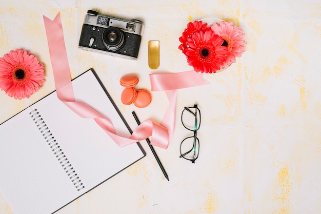 Foto gratuita cuaderno con cámara, flores y cinta en mesa de luz.