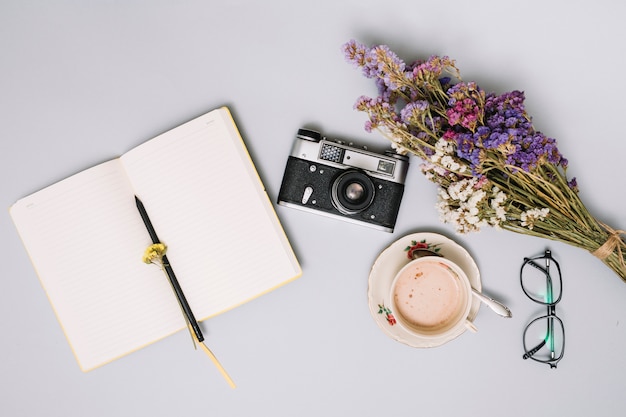 Cuaderno con camara y flores sobre mesa.