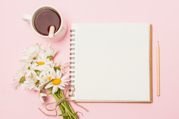 Cuaderno cerca de flores y copa de bebida.