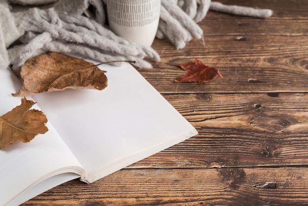 Cuaderno cerca de hojas de otoño y bufanda sobre mesa