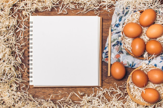 Cuaderno cerca de los huevos de gallina en cuencos en material floreado entre la malla a bordo