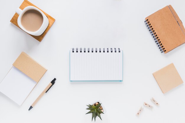 Cuaderno cerca de papelería, taza de café y macetas