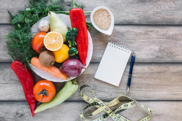 Cuaderno y cinta métrica cerca de verduras y frutas