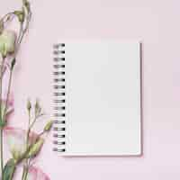 Foto gratuita cuaderno espiral en blanco con flores eustoma contra telón de fondo rosa