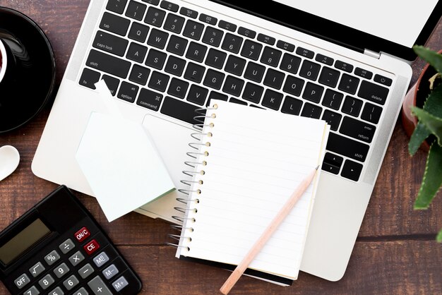 Cuaderno espiral en blanco con lápiz sobre una computadora portátil abierta en mesa de madera