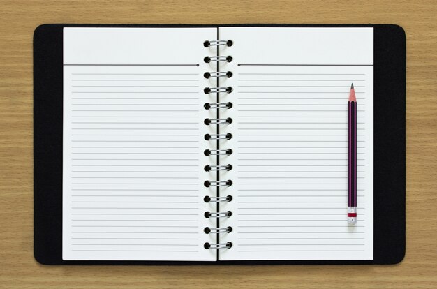 Cuaderno espiral en blanco y lápiz sobre fondo de madera
