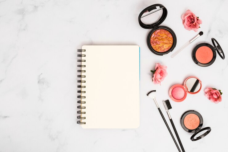 Foto gratuito cuaderno espiral en blanco con rosas rosadas; pinceles de maquillaje y polvos compactos.