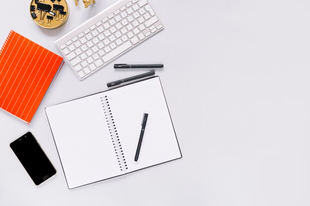 Cuaderno espiral y pluma con teléfono móvil y teclado sobre fondo blanco