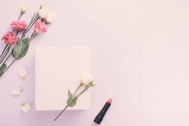 Cuaderno con flores color de rosa y lápiz labial en la mesa