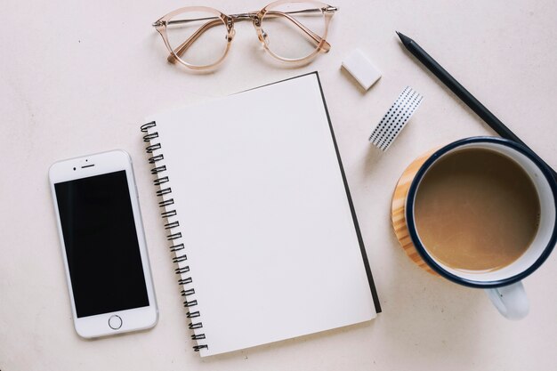 Cuaderno y gafas cerca de teléfono inteligente y café