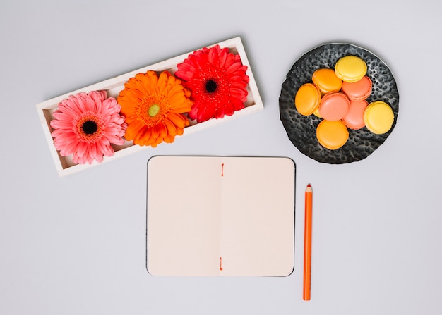 Cuaderno con galletas y flores brillantes en mesa blanca