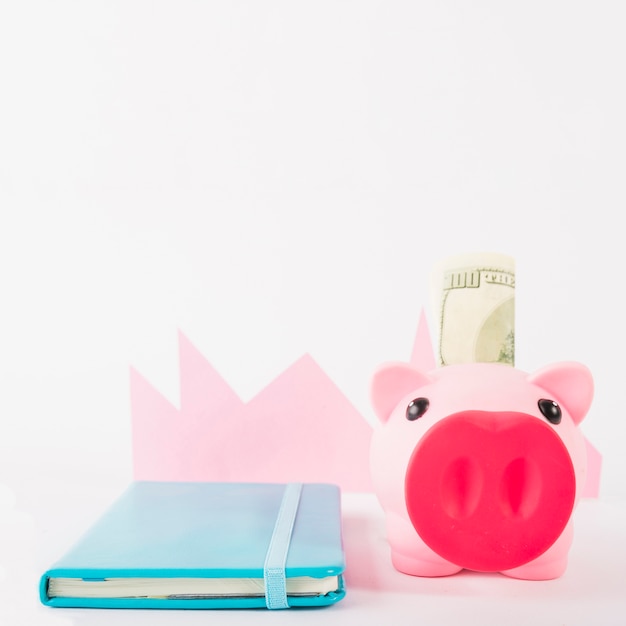 Cuaderno y hucha con dinero en fondo blanco