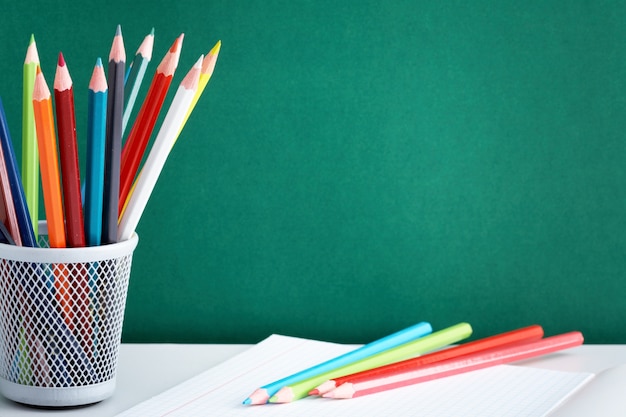 Cuaderno y lápices de colores con la pizarra de fondo