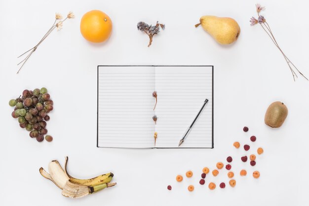 Cuaderno de una línea con cuaderno; bolígrafo; cuerno; frutas Café y flores secas sobre fondo blanco.