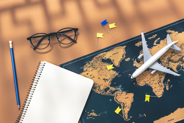Un cuaderno en miniatura de avión y un mapa del mundo sobre fondo marrón plano