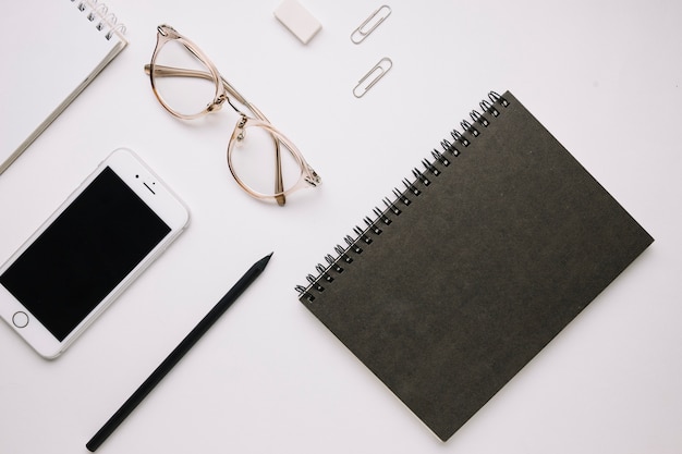 Cuaderno negro cerca de teléfono inteligente y papelería