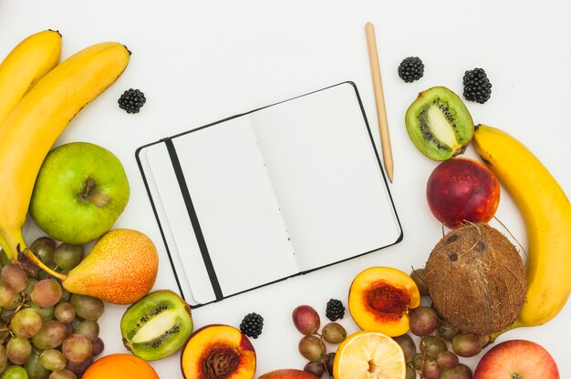 Un cuaderno de páginas en blanco abierto; Lápiz y muchas frutas sobre fondo blanco