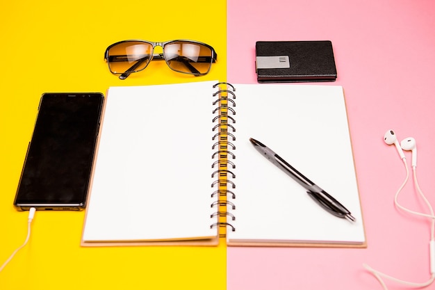 Cuaderno de papel, teléfono inteligente, gafas de sol y soporte para tarjetas de visita sobre fondo de dos colores