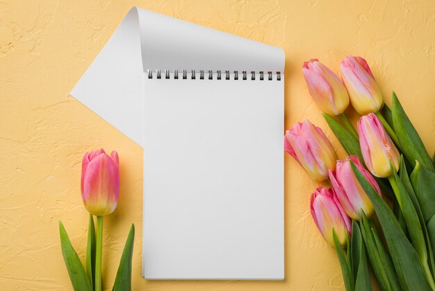 Cuaderno plano al lado de tulipanes