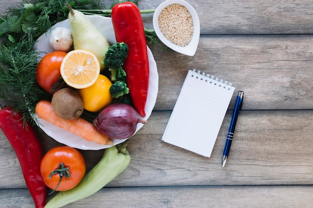 Cuaderno y pluma cerca de frutas y verduras