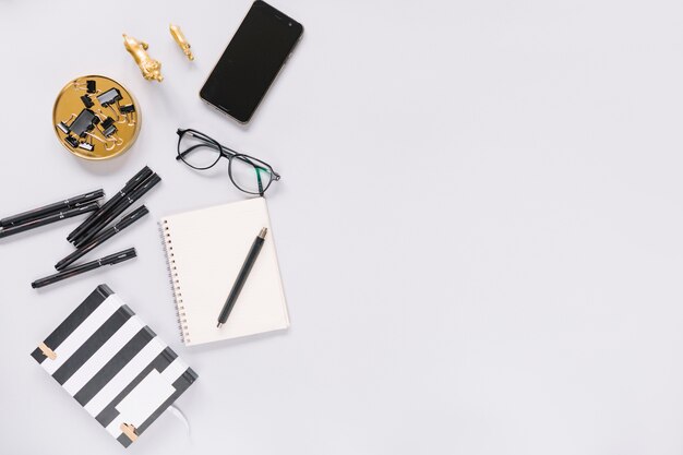 Cuaderno; rotulador; los anteojos; papelería y teléfono celular en el fondo blanco