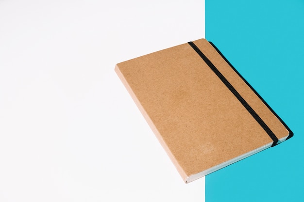 Cuaderno de tapa marrón sobre fondo blanco y azul